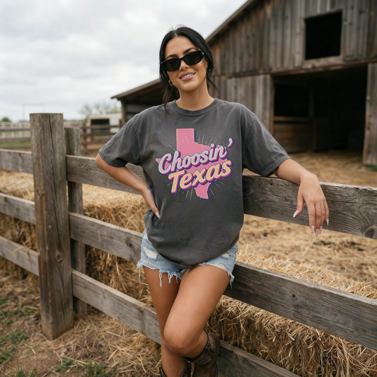 Woman wearing charcoal Choosin Texas pink western graphic tee with denim shorts and cowboy boots at rustic barn