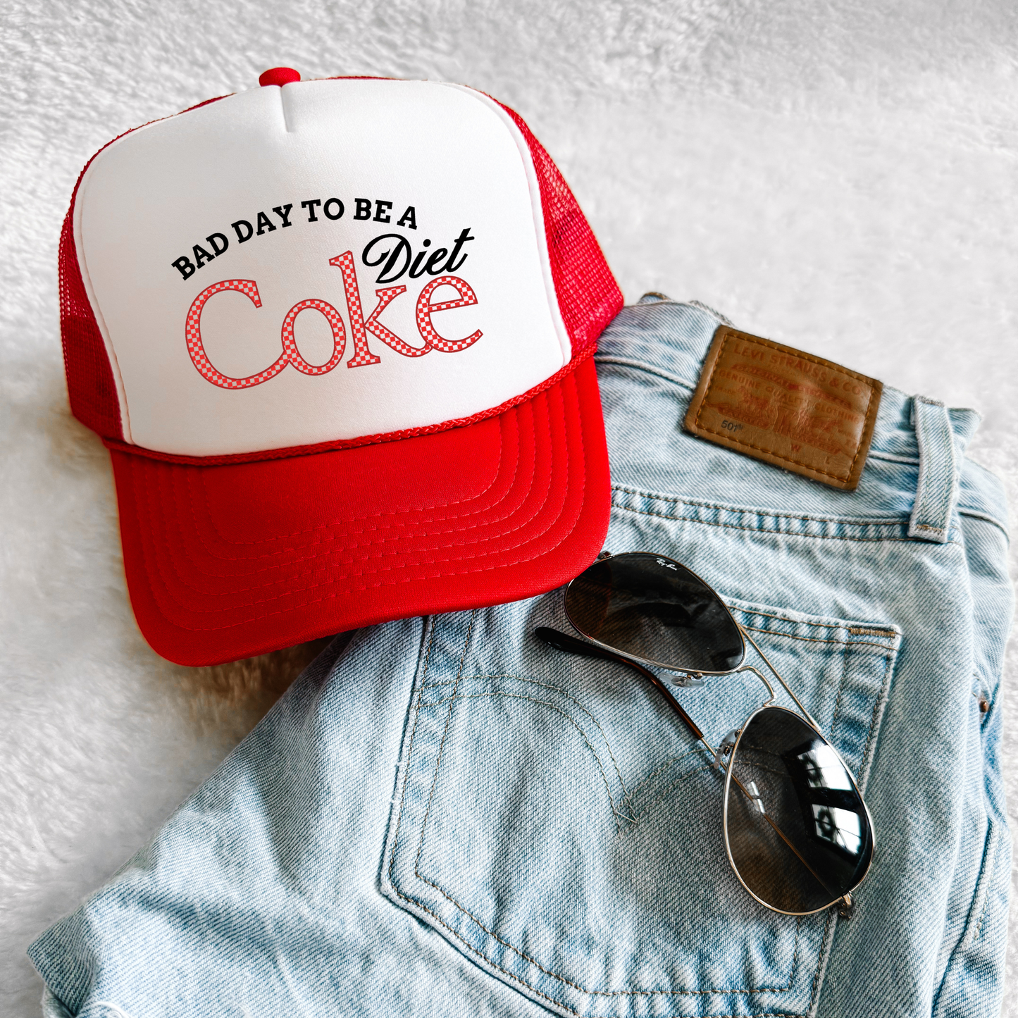 Red and white foam trucker hat with “Bad Day to Be a Diet Coke” retro graphic styled with denim and sunglasses