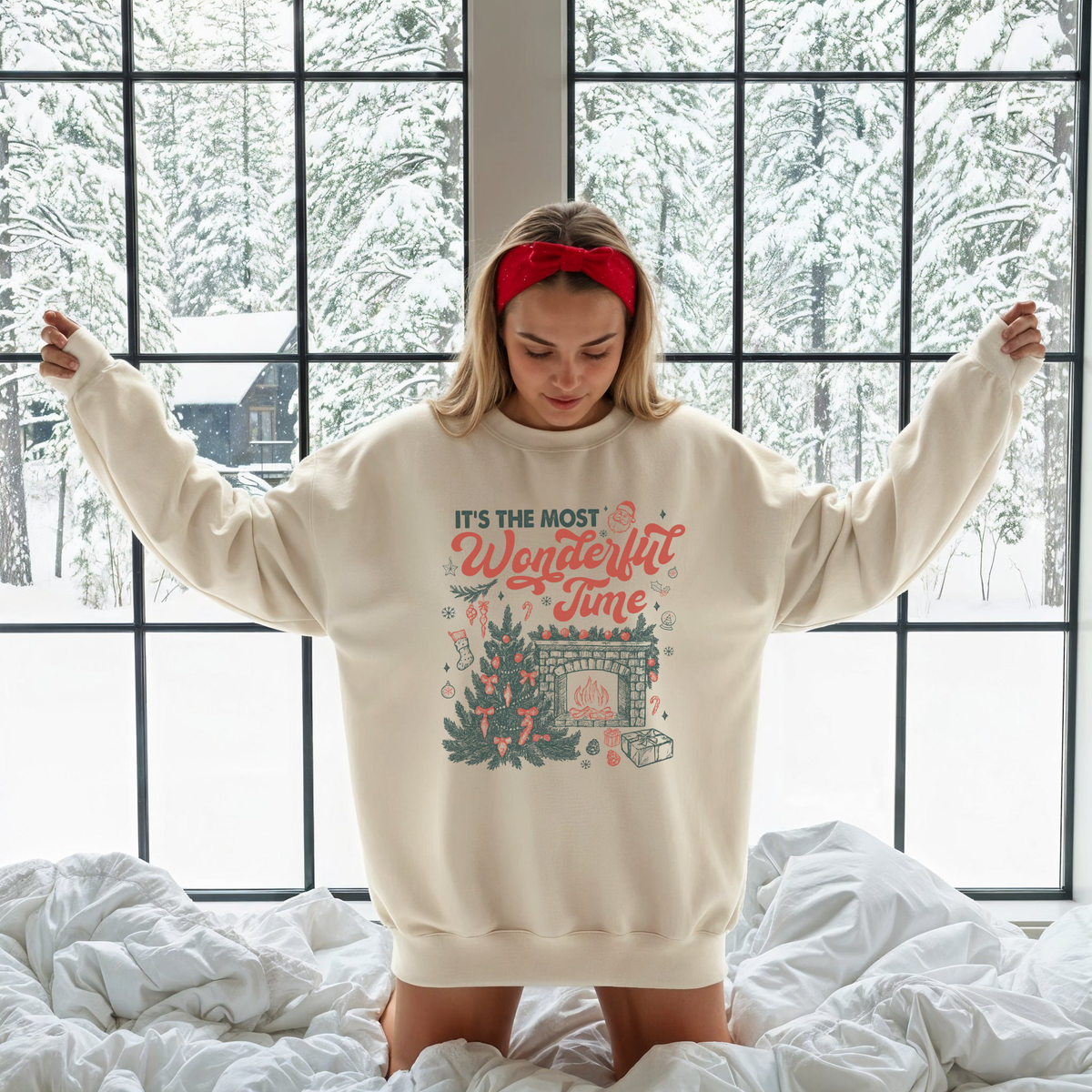 Woman wearing an off-white “It’s the Most Wonderful Time” Christmas sweatshirt, standing in front of a snowy window with cozy holiday decor.