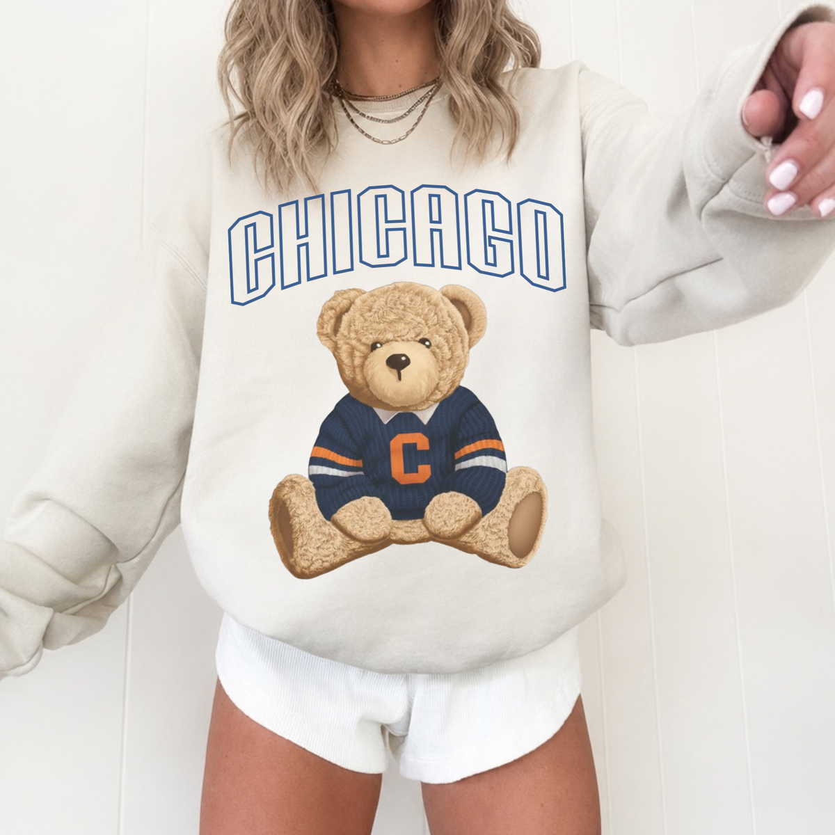 Woman styling a sand-colored Chicago vintage teddy bear sweatshirt with layered necklaces and white shorts