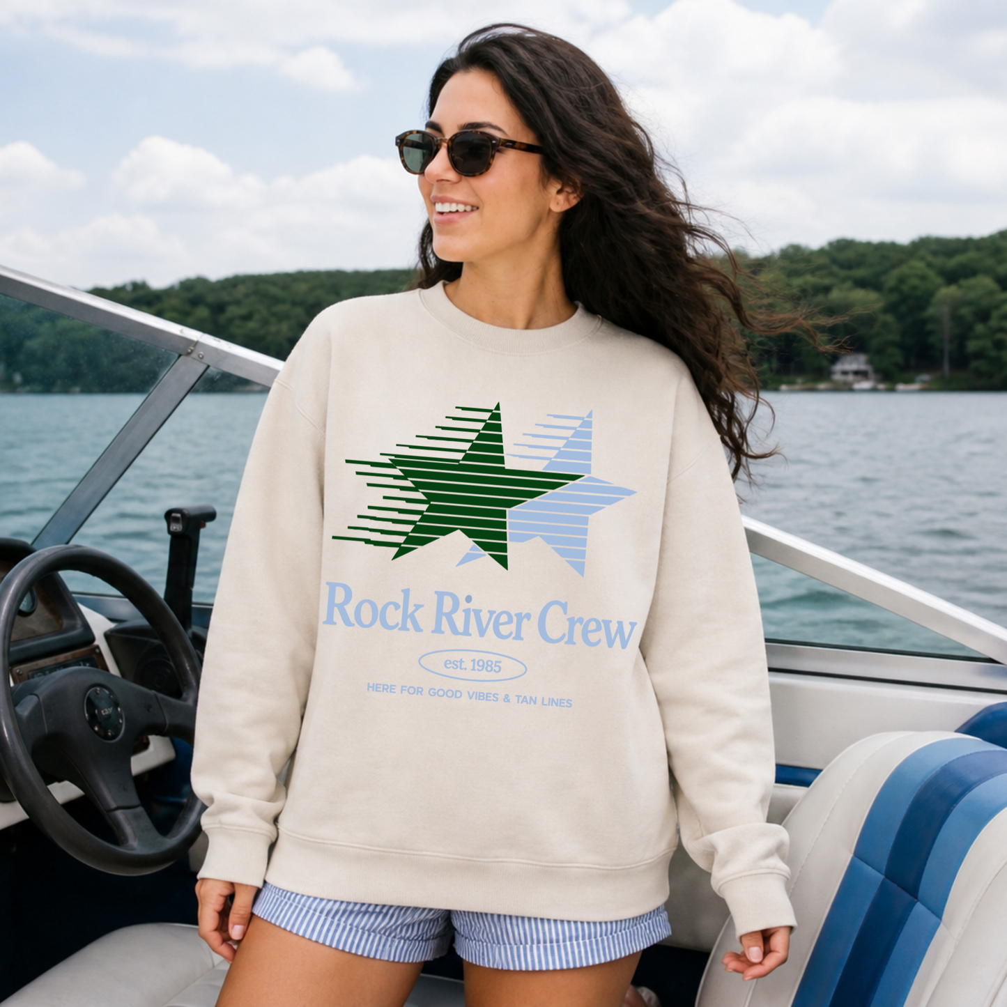 Woman wearing a 'Rock River Crew' sweatshirt on a boat by a lake.