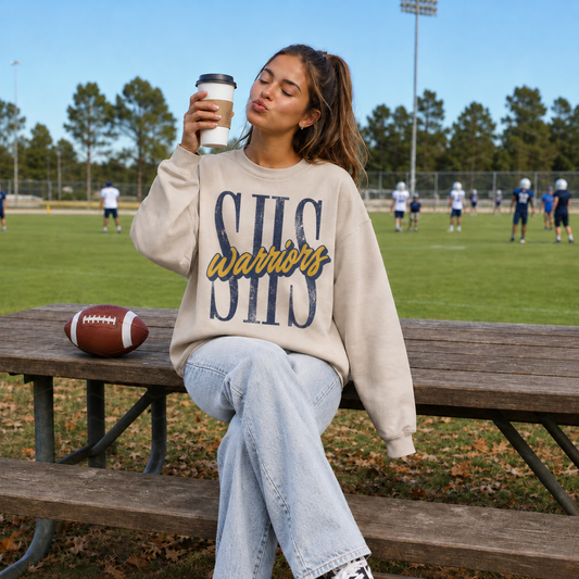 Woman wearing a Sterling Warriors SHS graphic sweatshirt at a football field featuring oversized distressed SHS lettering with navy and gold Warriors script.