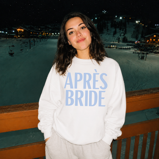 Bride wearing white Après Bride crewneck sweatshirt at snowy ski resort