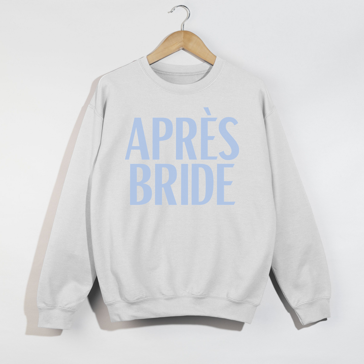 White Après Bride sweatshirt with blue lettering displayed on wooden hanger