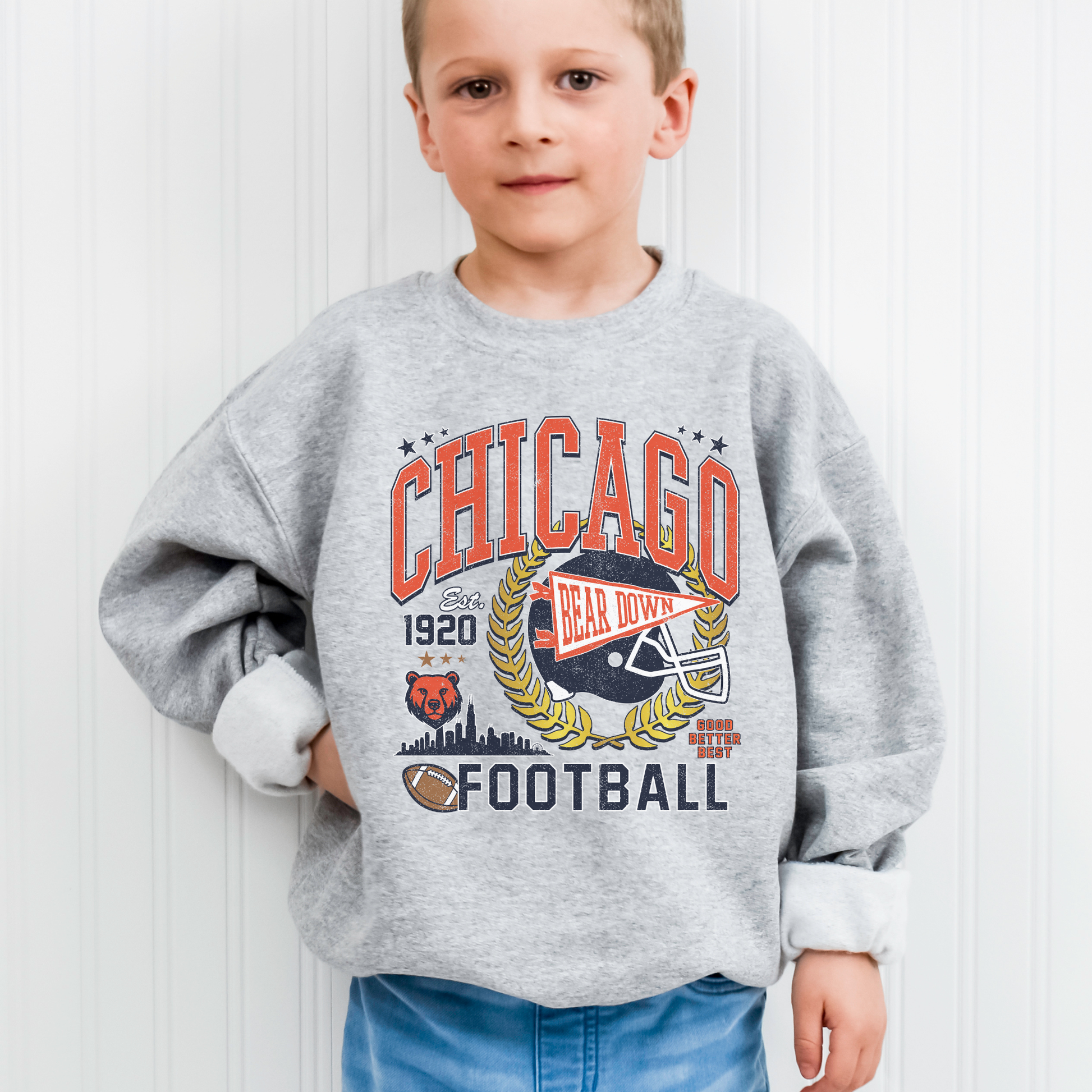 Child wearing a gray sweatshirt with 'Chicago Football' design against a white wall.