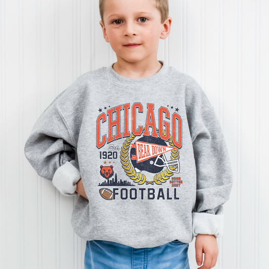 Child wearing a gray sweatshirt with 'Chicago Football' design against a white wall.