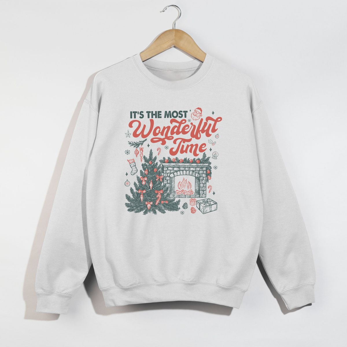 White crewneck sweatshirt on hanger featuring “It’s the Most Wonderful Time” holiday design with tree and fireplace graphic.
