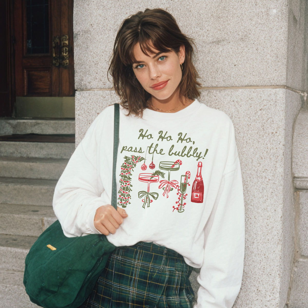 Woman in white “Ho Ho Ho, Pass the Bubbly!” sweatshirt with festive drink illustrations, smiling in front of stone steps.