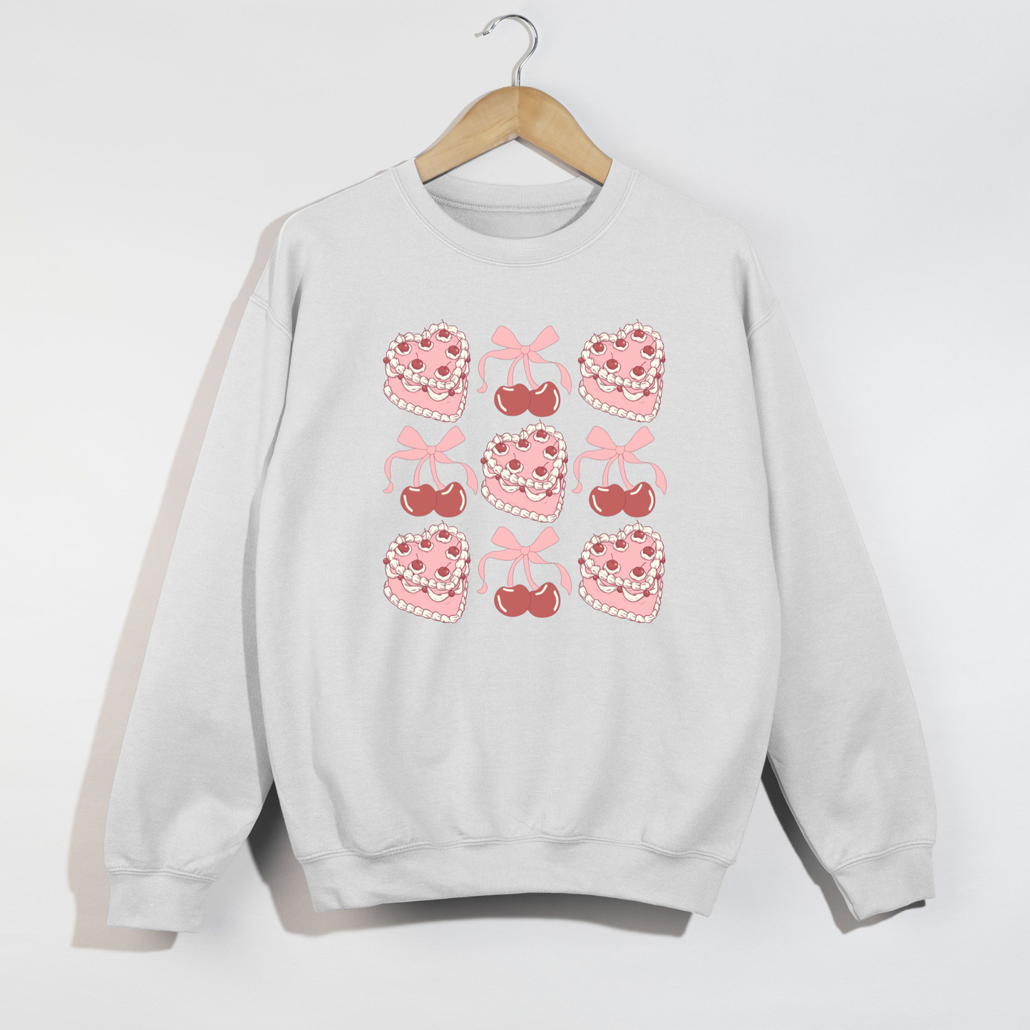 White Valentine sweatshirt on hanger featuring pink heart cakes, cherries, and bow illustrations in a 3x3 grid design.