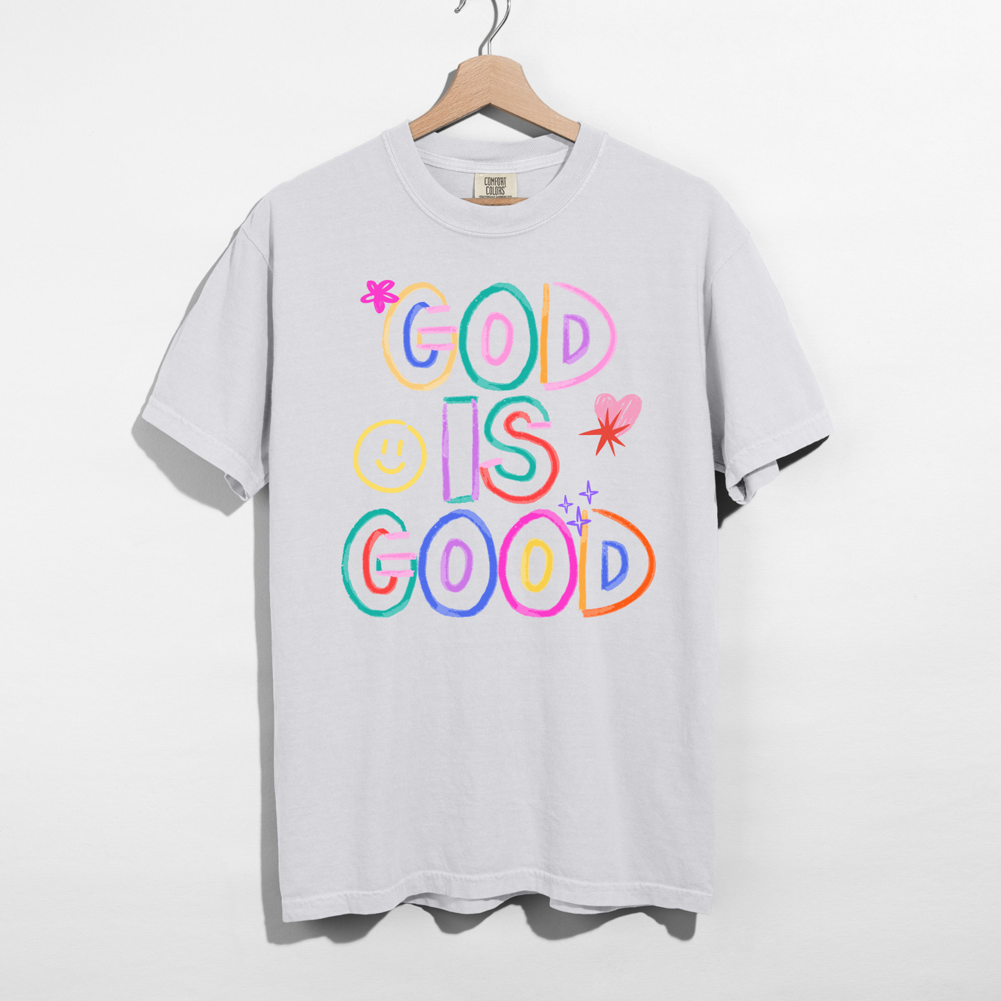 White t-shirt with 'God is Good' text in colorful letters on a hanger against a white background