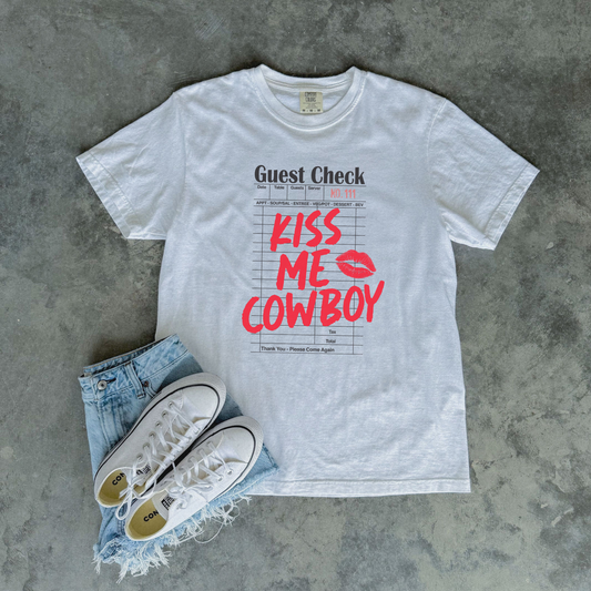 Flat lay of Kiss Me Cowboy western graphic tee with denim and sneakers