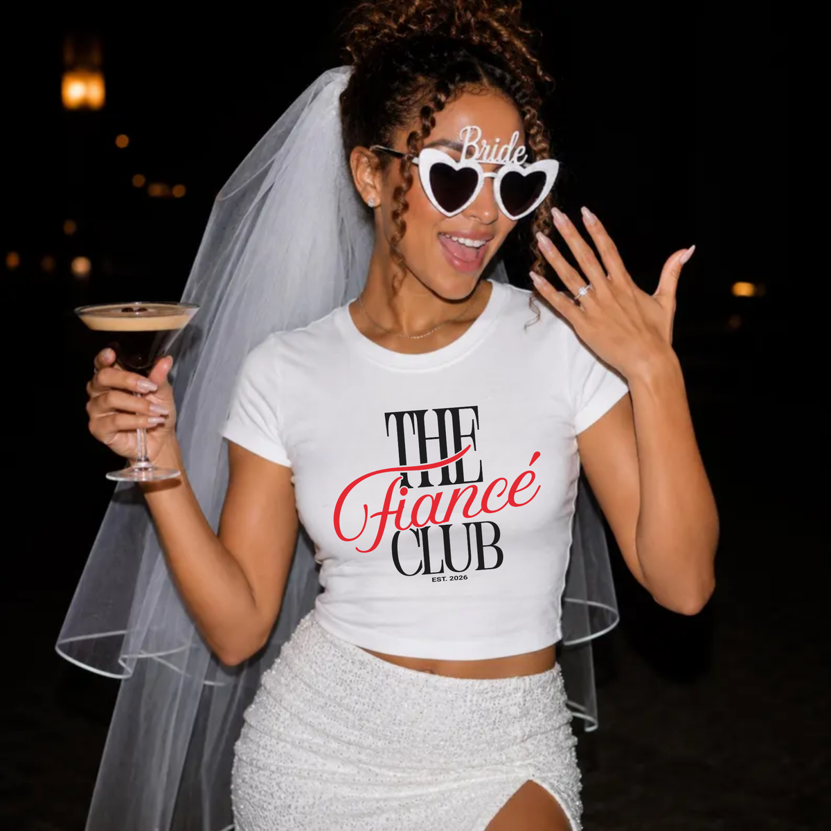 Newly engaged bride wearing The Fiancé Club Est. 2026 shirt showing engagement ring