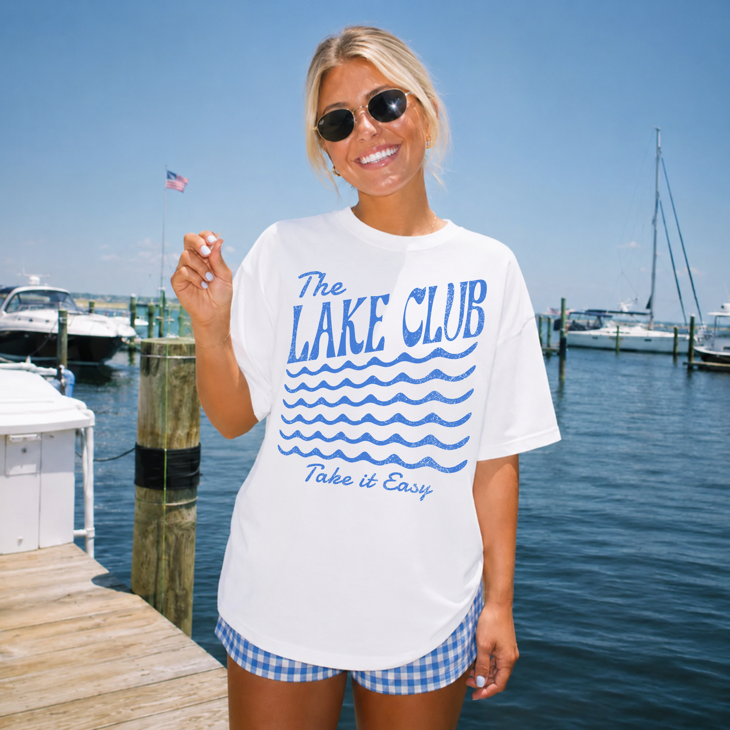 Woman wearing The Lake Club Take It Easy graphic t-shirt on a marina dock with boats and waterfront background