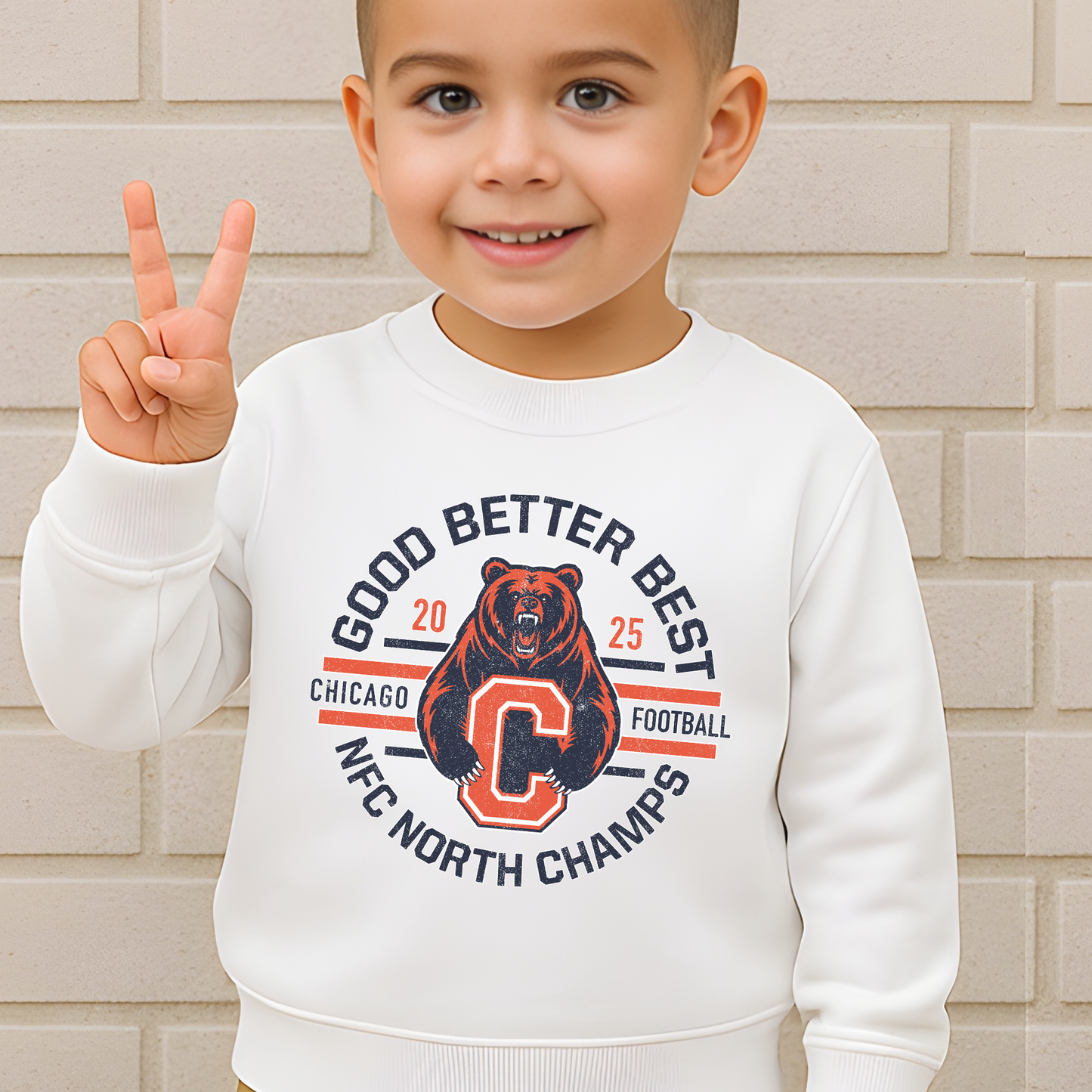 Child wearing a white sweatshirt with a bear graphic and text, standing against a beige brick wall.