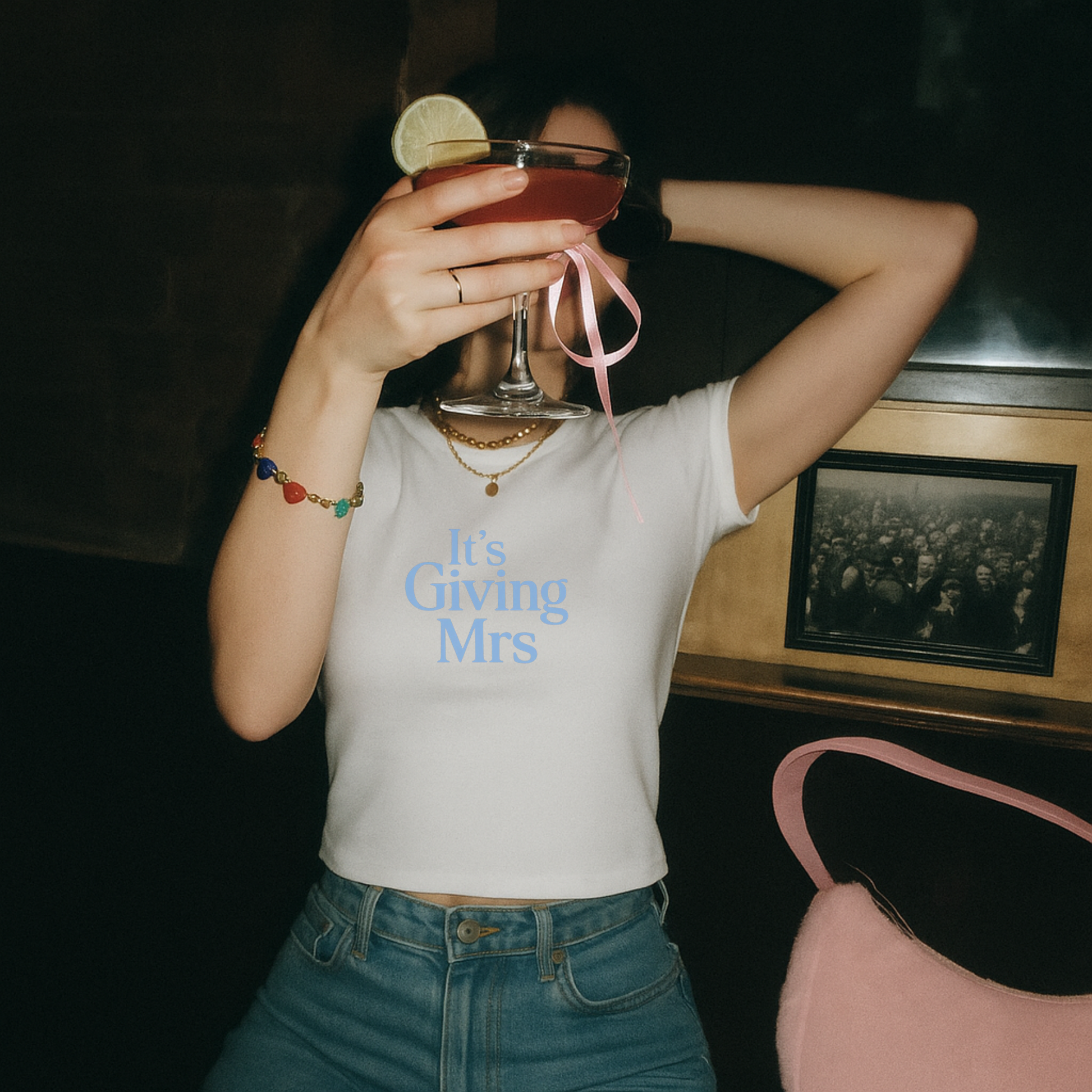 Bride wearing white “It’s Giving Mrs” graphic tee while holding cocktail