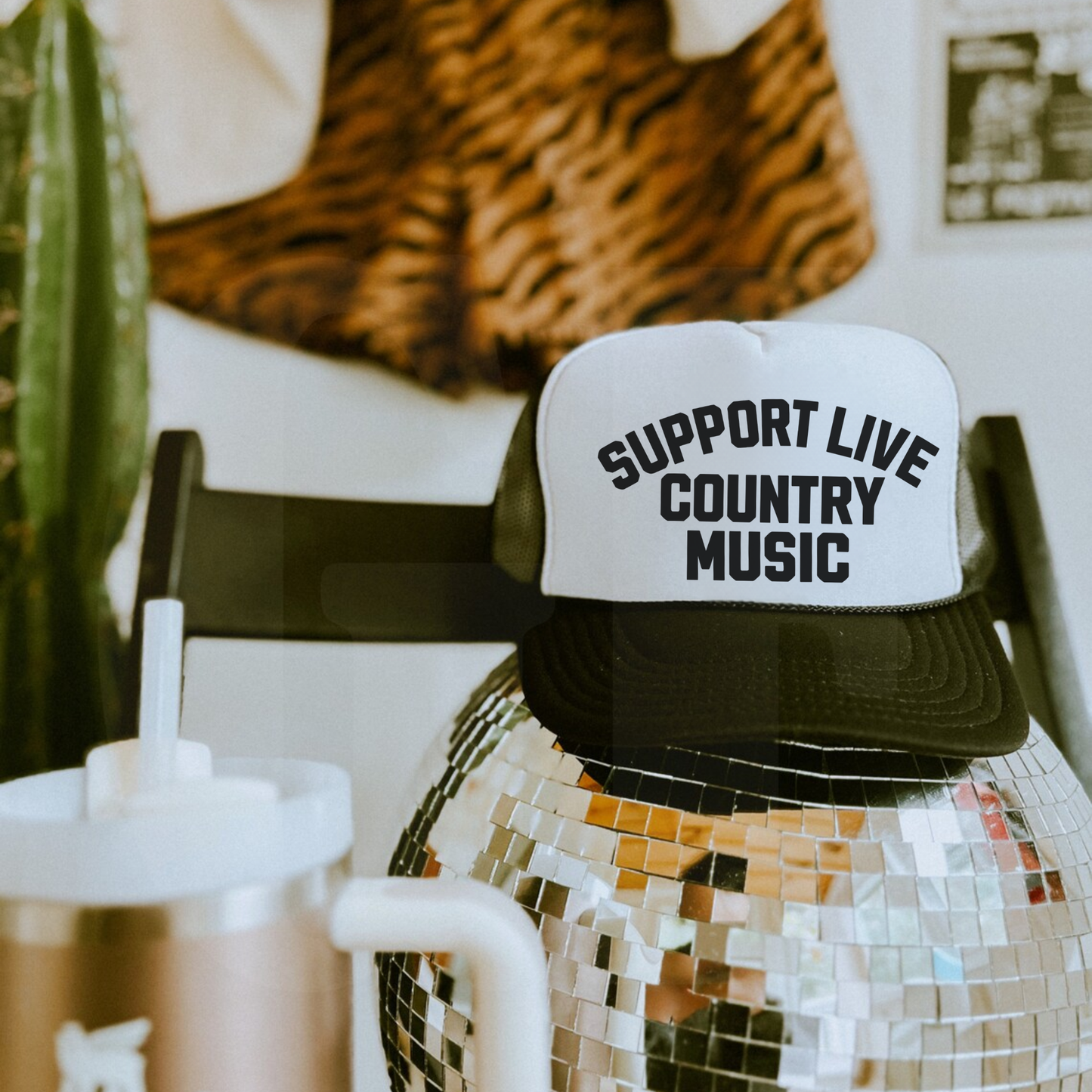 Black and white Support Live Country Music trucker hat displayed on disco ball with western-inspired decor