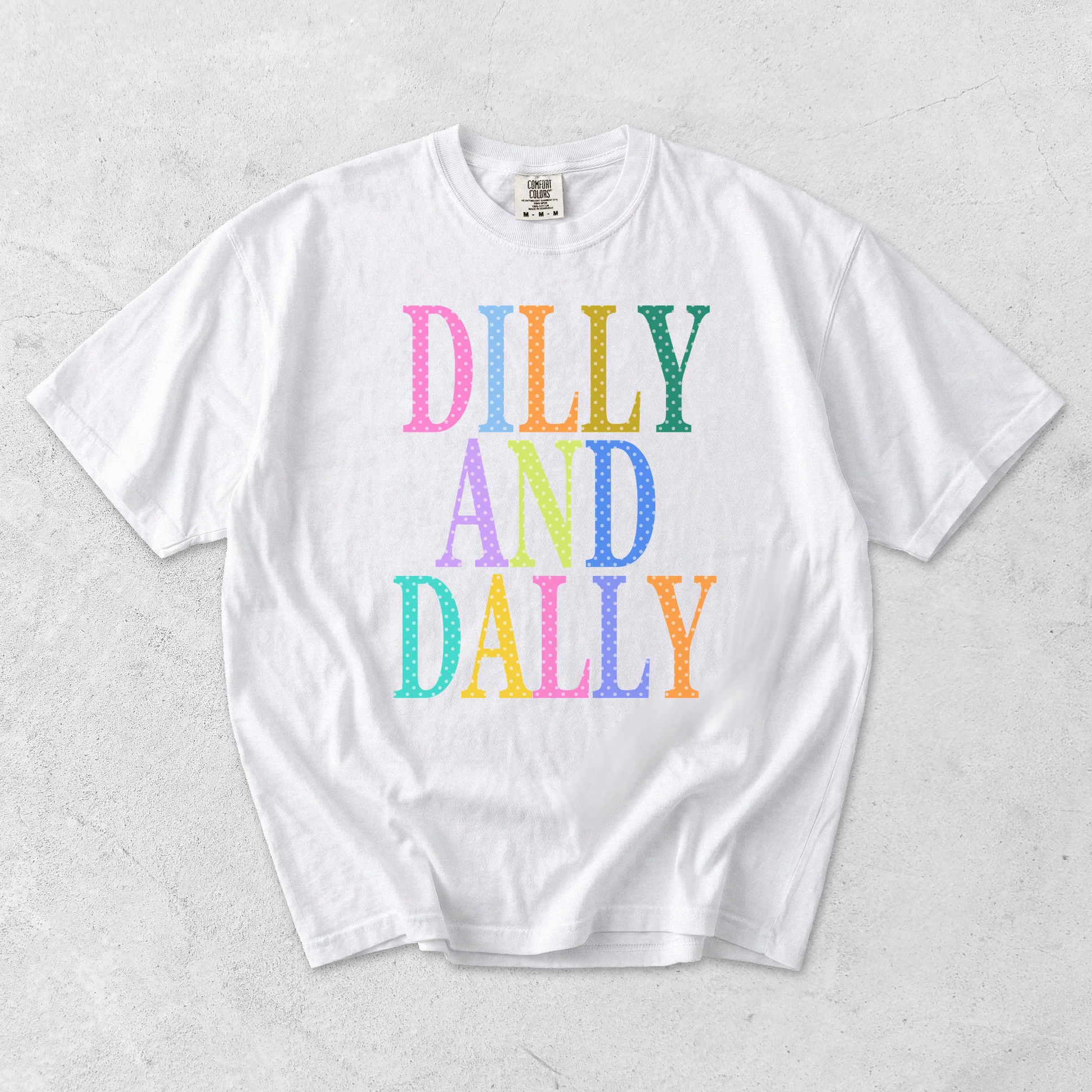 White Comfort Colors Dilly and Dally colorful retro graphic tee flat lay on textured background