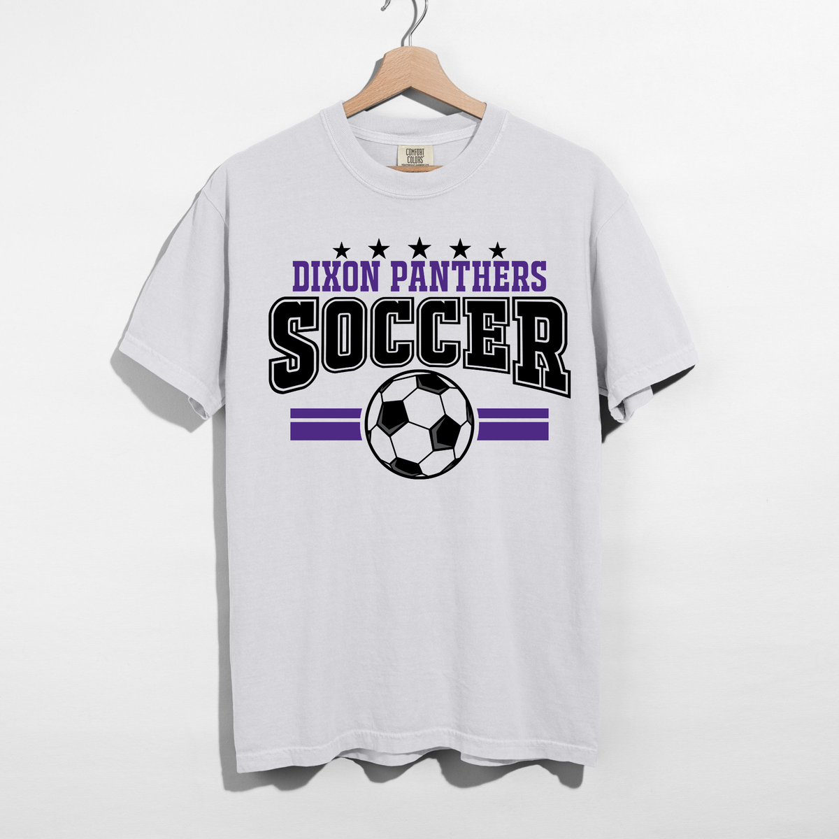 A white short-sleeve t-shirt hanging on a wooden hanger against a white wall. The shirt features a graphic print for 'Dixon Panthers Soccer' with purple and black lettering, stars, stripes, and a soccer ball.