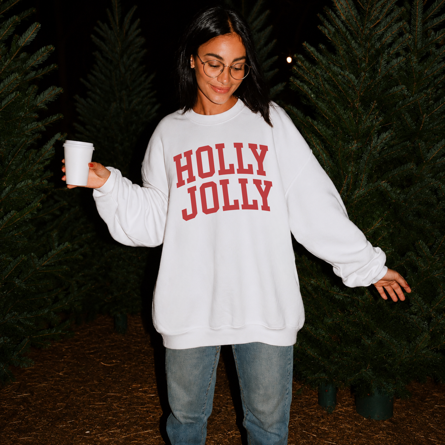 Woman wearing a white Holly Jolly Christmas crewneck sweatshirt with red varsity lettering at a Christmas tree farm.