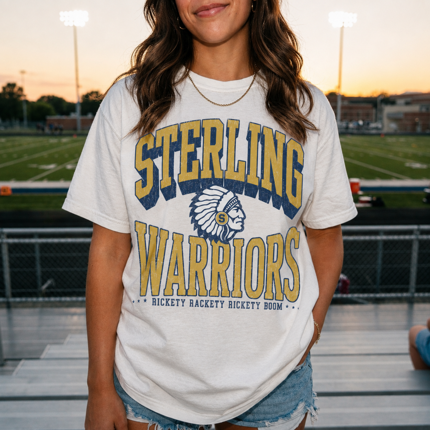 Woman wearing an ivory Vintage Sterling Warriors Football graphic tee featuring distressed navy and gold varsity artwork, styled for Sterling High School game day.