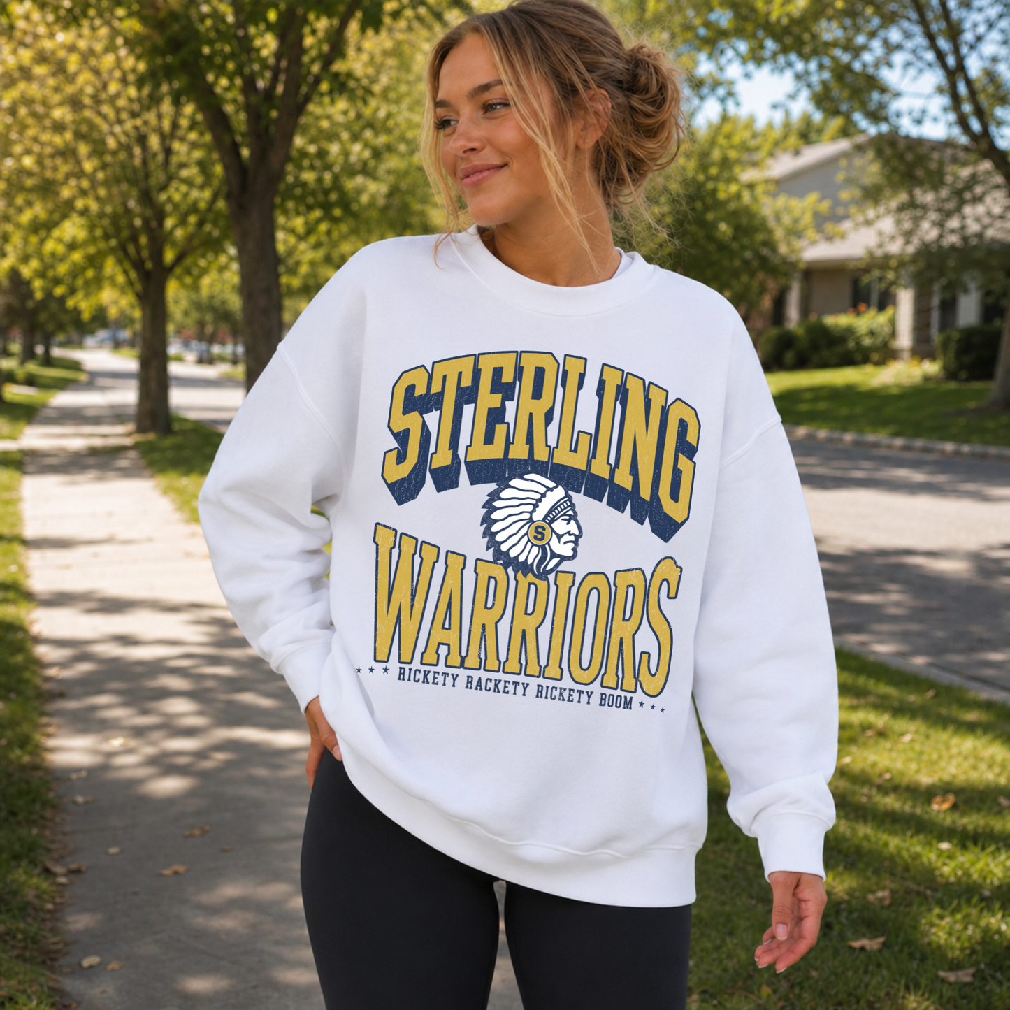 Woman wearing a white Sterling Warriors sweatshirt featuring vintage collegiate lettering, Warrior mascot, and Rickety Rackety Rickety Boom cheer while walking outdoors.
