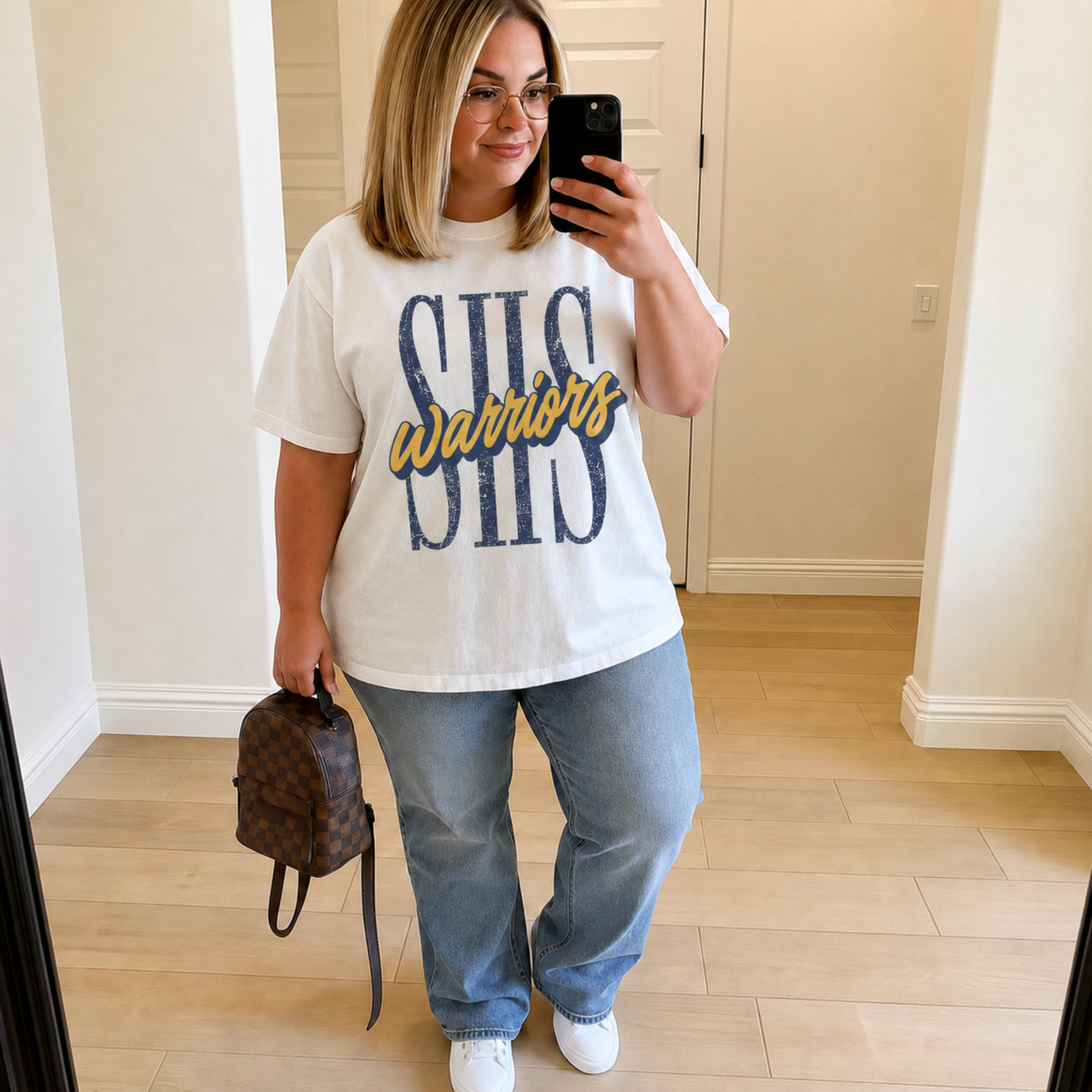 Woman wearing a white SHS Warriors graphic tee featuring distressed navy SHS lettering with gold Warriors script, styled with light wash jeans for Sterling Warriors game day.