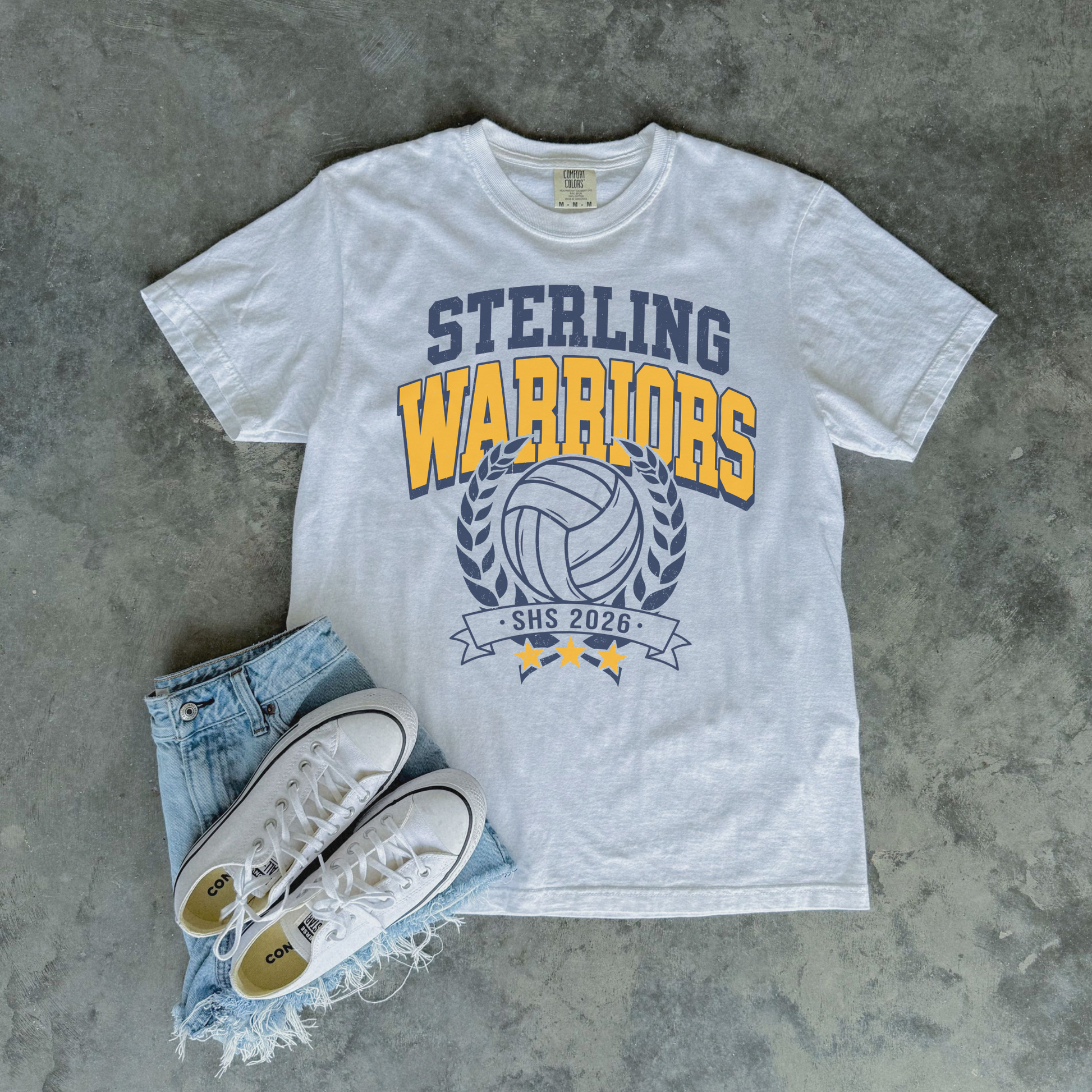 White Sterling Warriors Volleyball Comfort Colors graphic t-shirt flat lay with denim shorts and white sneakers featuring varsity volleyball design.