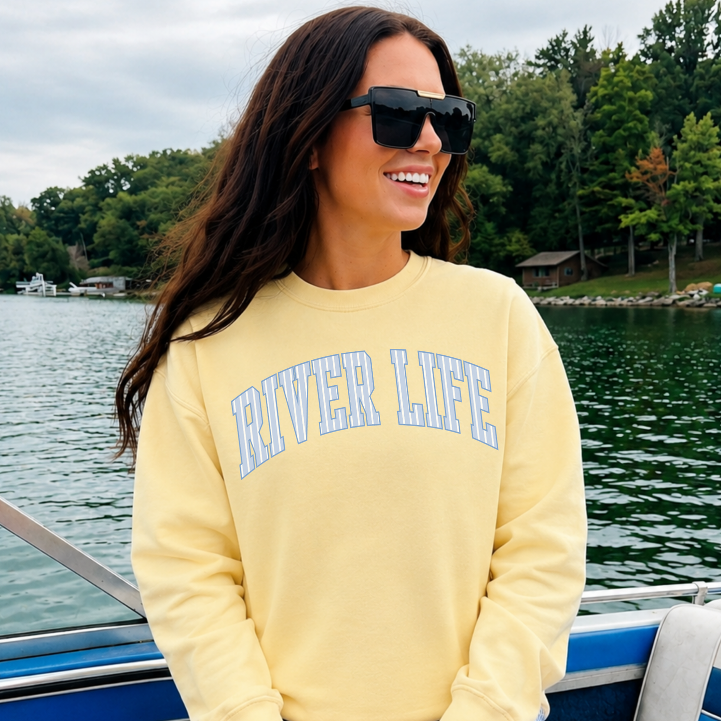 woman wearing butter yellow river life sweatshirt with blue collegiate lettering on boat close up river lifestyle image